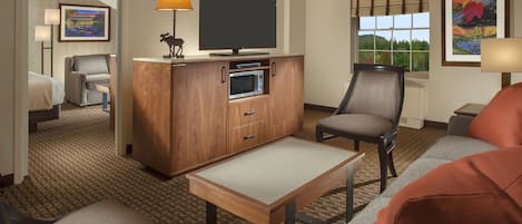 Una habitación de hotel con una televisión de pantalla plana, un mueble de madera con microondas, un sofá, una silla y una pequeña mesa.