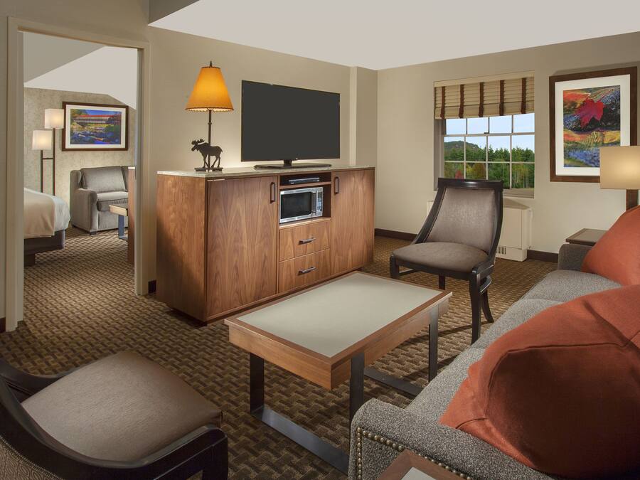 Une chambre d’hôtel équipée d’un téléviseur à écran plat, d’un meuble en bois contenant un four à micro-ondes, d’un canapé, d’une chaise et d’une petite table.