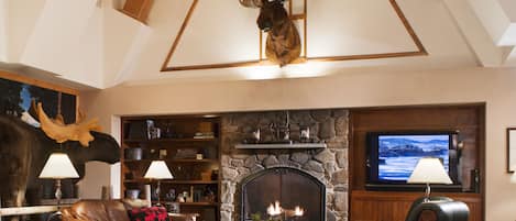 Un salón amplio con chimenea, muebles de cuero y una cabeza de ciervo montada.