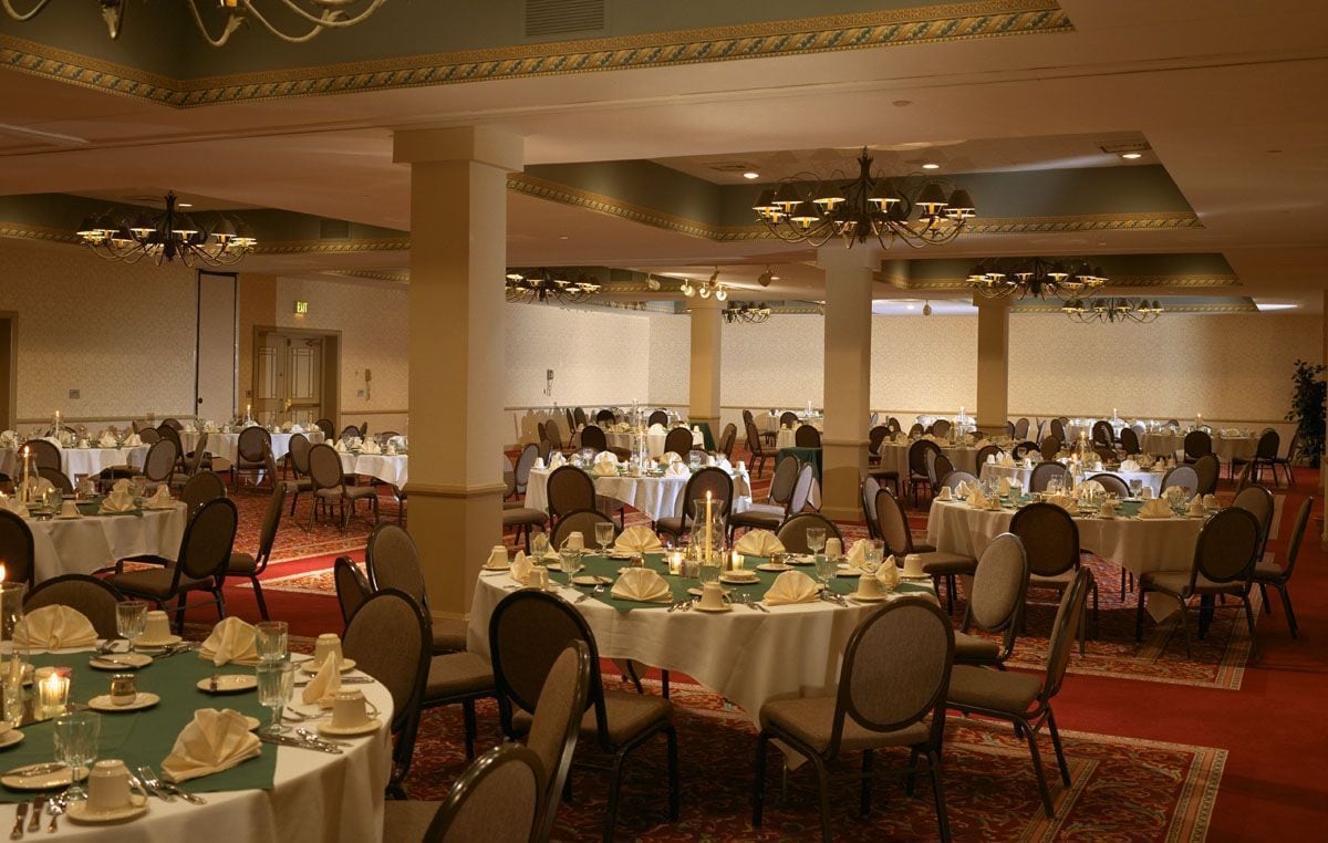 A banquet hall with round tables set for dining, featuring white tablecloths and formal table settings.