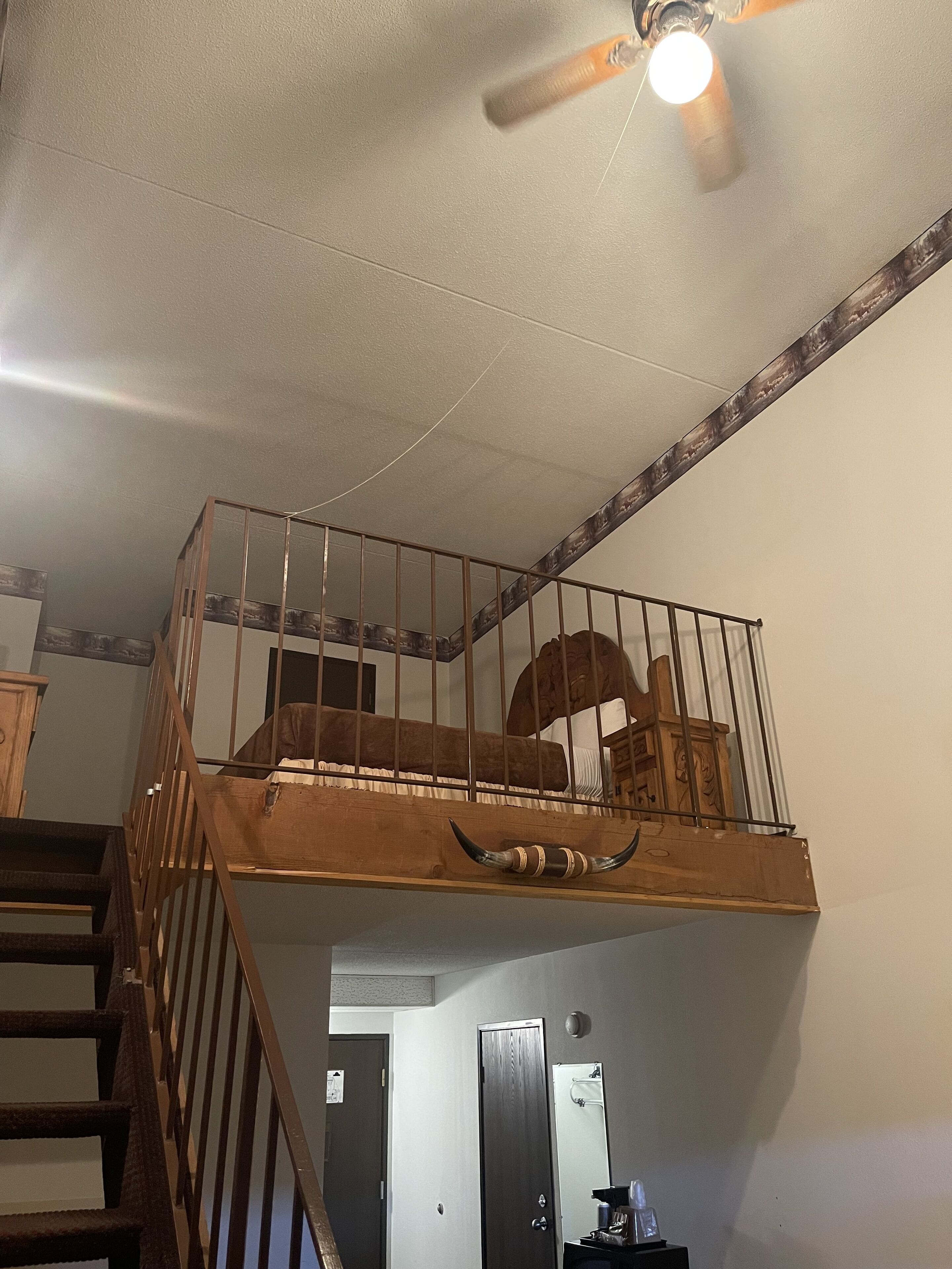 A multi-level room with a wooden staircase, a ceiling fan, and a bunk bed on the upper level.