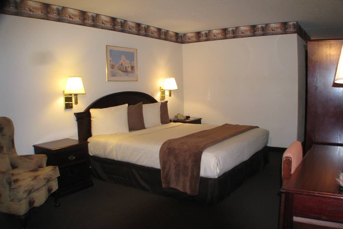 Une chambre d’hôtel avec un grand lit, deux lampes de chevet, une chaise, un bureau et un tableau au mur.