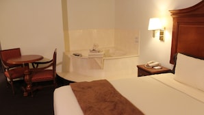 Une chambre d’hôtel avec un lit, une chaise, une petite table, un bureau, une lampe et une baignoire.