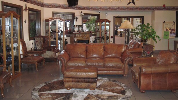 Un salon spacieux avec un grand canapé en cuir marron, un pouf assorti et un lustre.