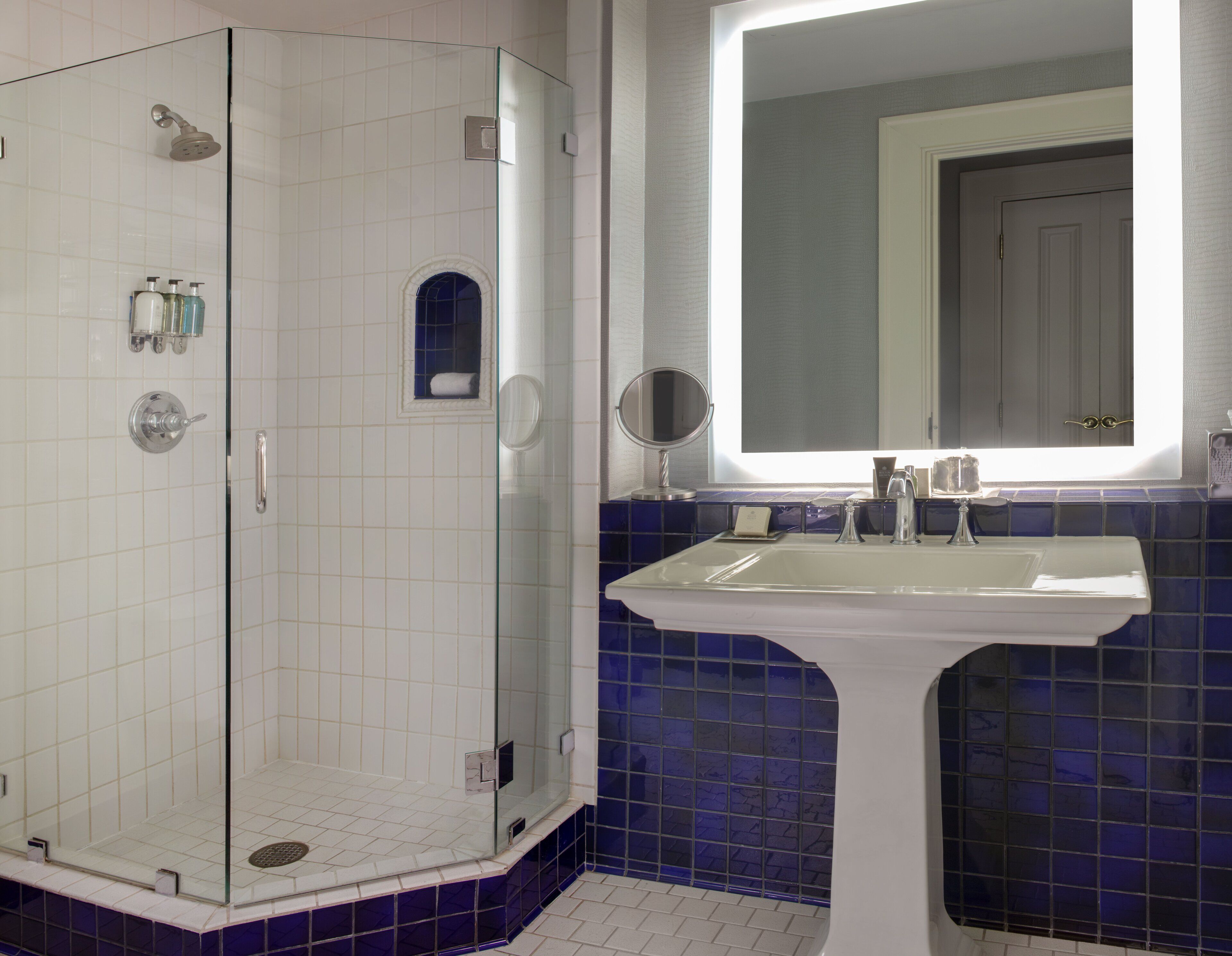 Een badkamer met een douchecabine van glas, een wastafel met spiegel en blauwe betegelde wanden.