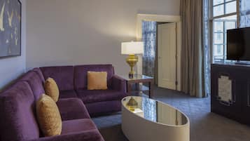 A modern living room with a purple sofa, patterned cushions, a glass coffee table, a lamp, and a TV.