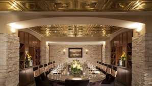 Comedor formal con pared de piedra, candelabro y una larga mesa dispuesta para una comida.