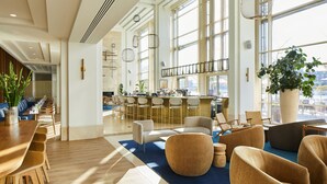 A spacious hotel lobby with a long dining area, comfortable seating, a bar, and large windows offering a view of the city. - Copenhagen Marriott Hotel (Copenhagen)