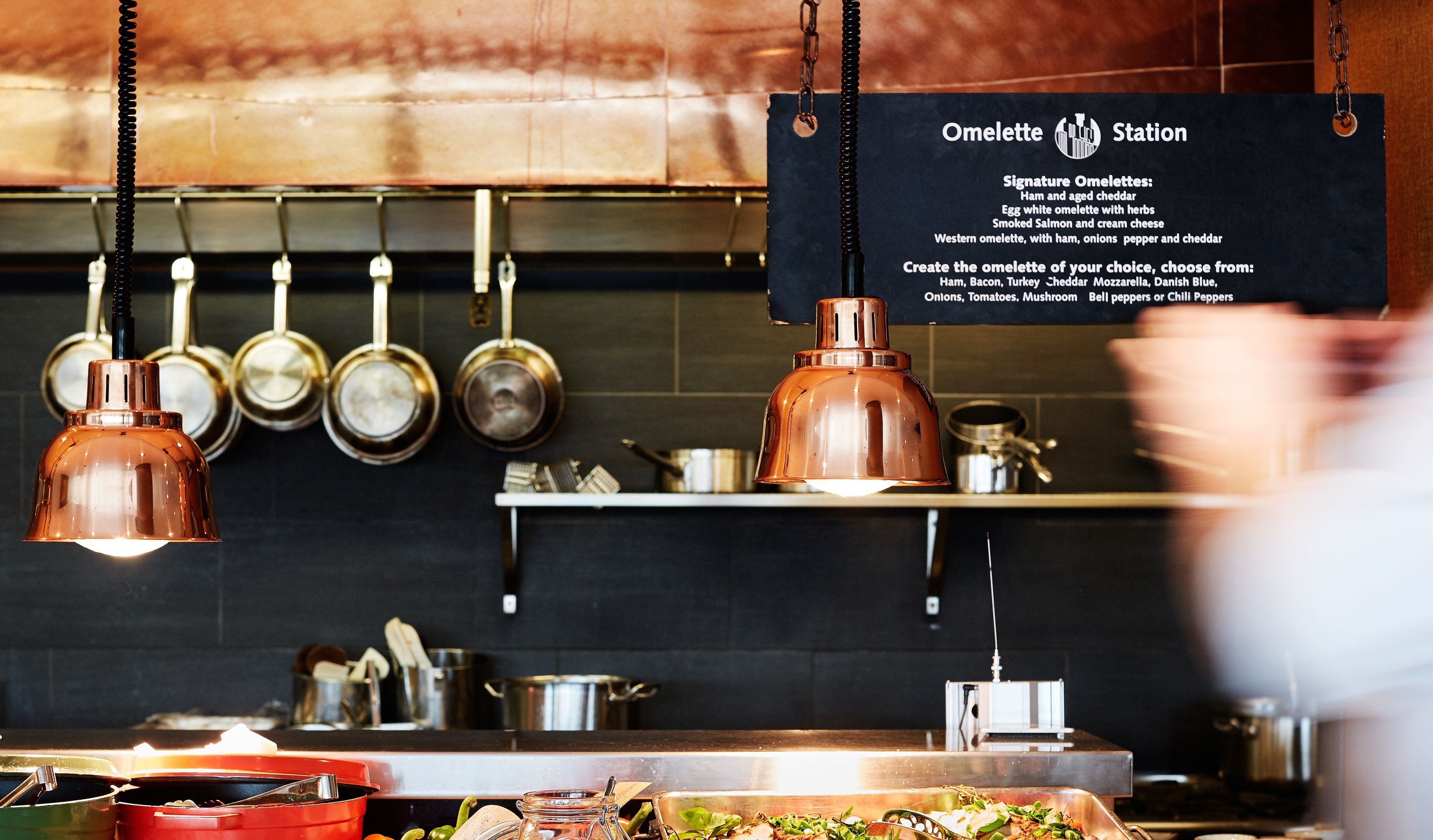 Une cuisine avec des casseroles suspendues, une bouilloire en cuivre et un tableau affichant le menu du coin où sont préparées les omelettes.