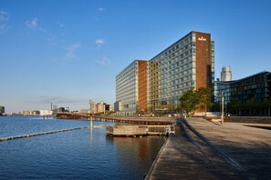 Een modern hotel met een grote glazen gevel, gelegen nabij een waterkant met een steiger.