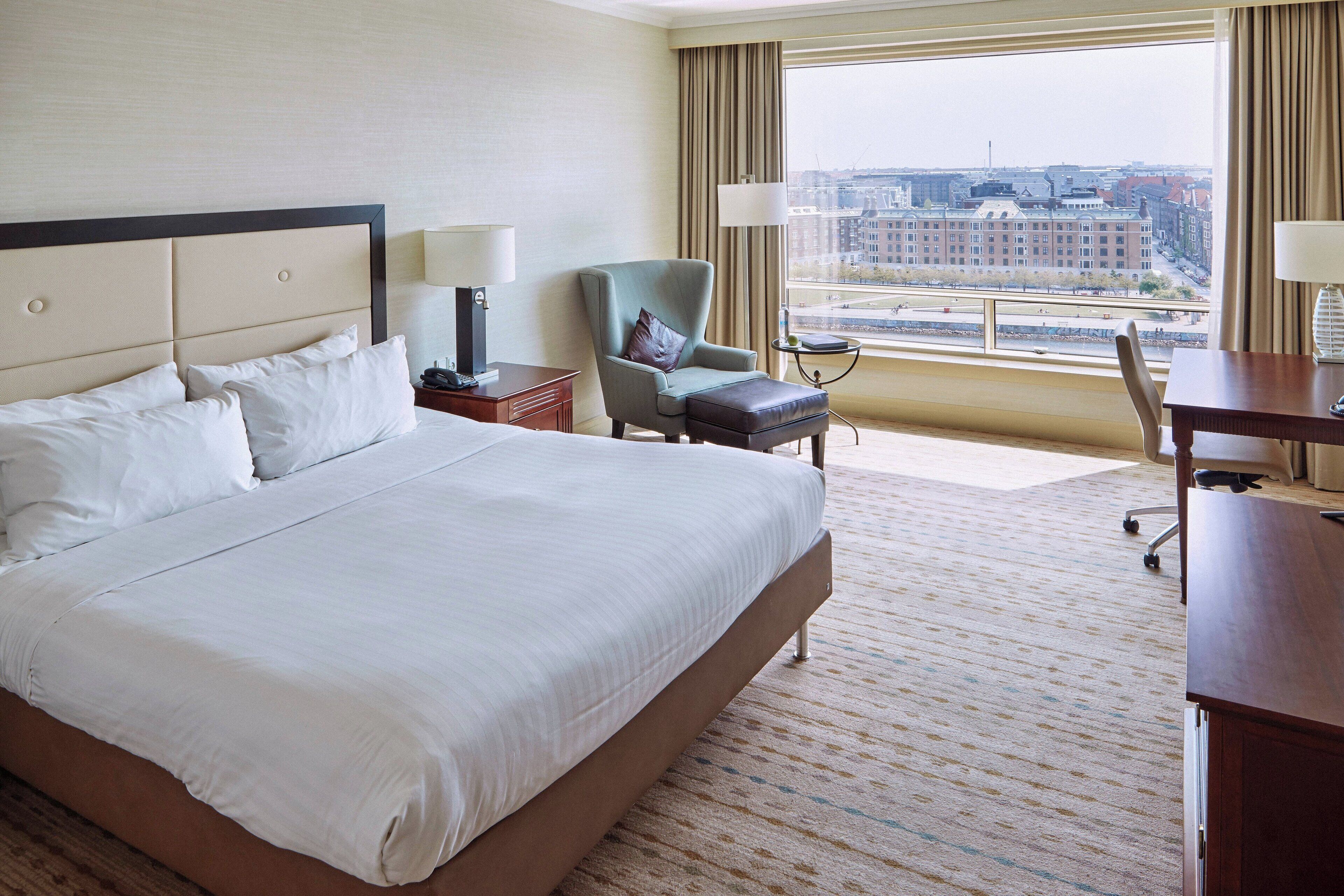 Een hotelkamer met een groot bed, een bureau, een stoel en uitzicht op de stad.