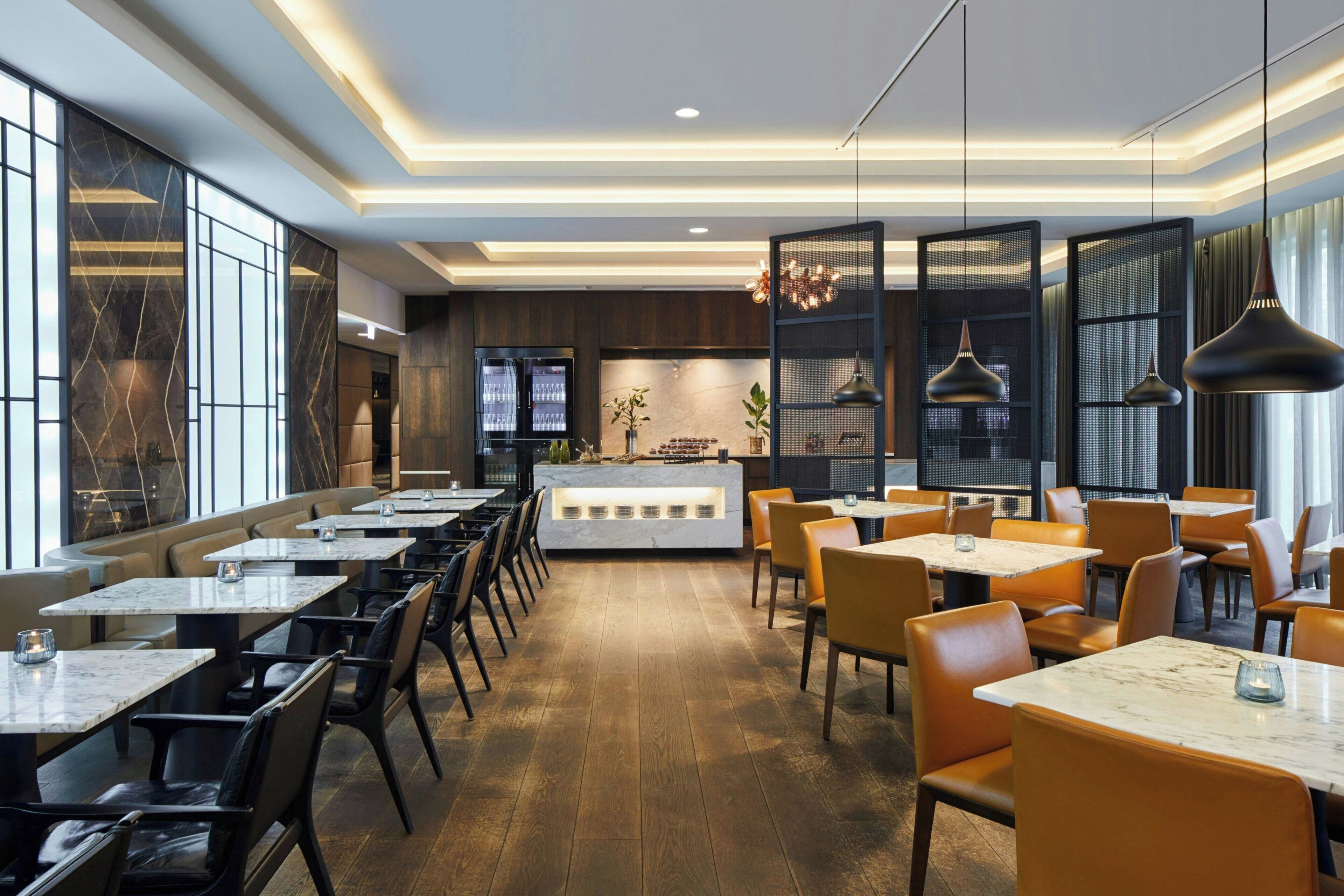 A modern restaurant with marble-topped tables and leather chairs, a central counter with a display, and a warm wooden floor.