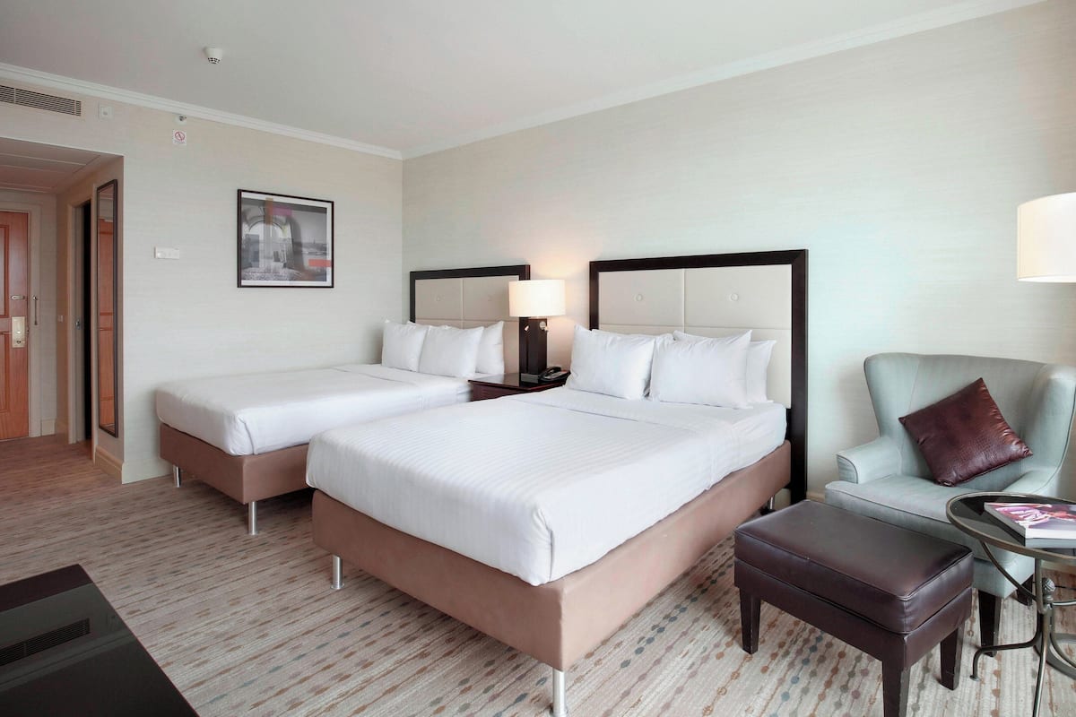 Una habitación de hotel con dos camas, una silla, una mesa y una lámpara.
