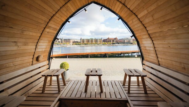A wooden pavilion with benches and a table, overlooking a river and buildings. - Copenhagen Marriott Hotel (Copenhagen)