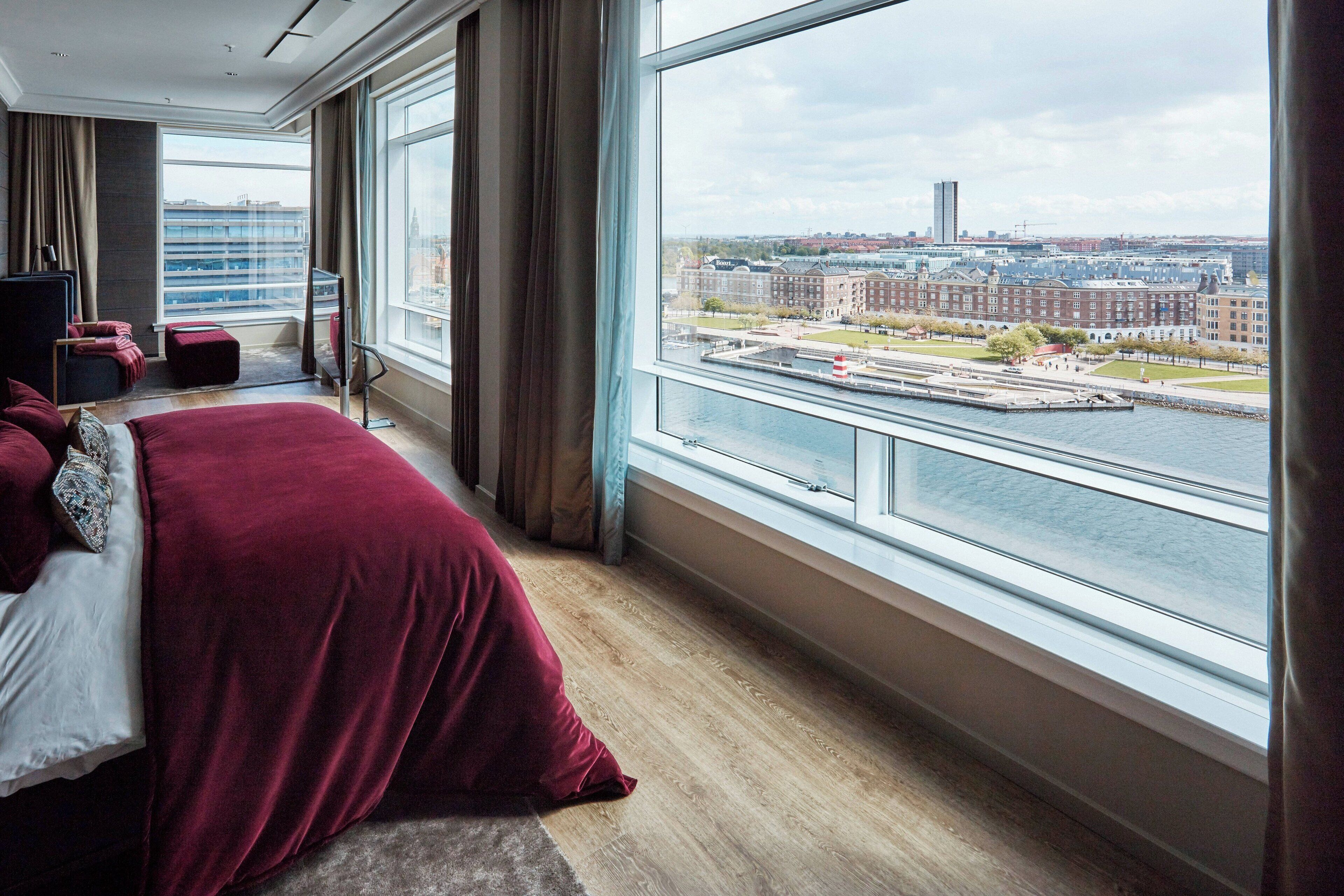 A modern hotel room with a large window offering a view of a cityscape and water.