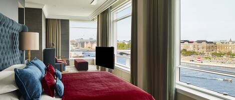 Habitación de hotel moderna con una cama grande, televisión de pantalla plana y vistas a la ciudad y al agua.