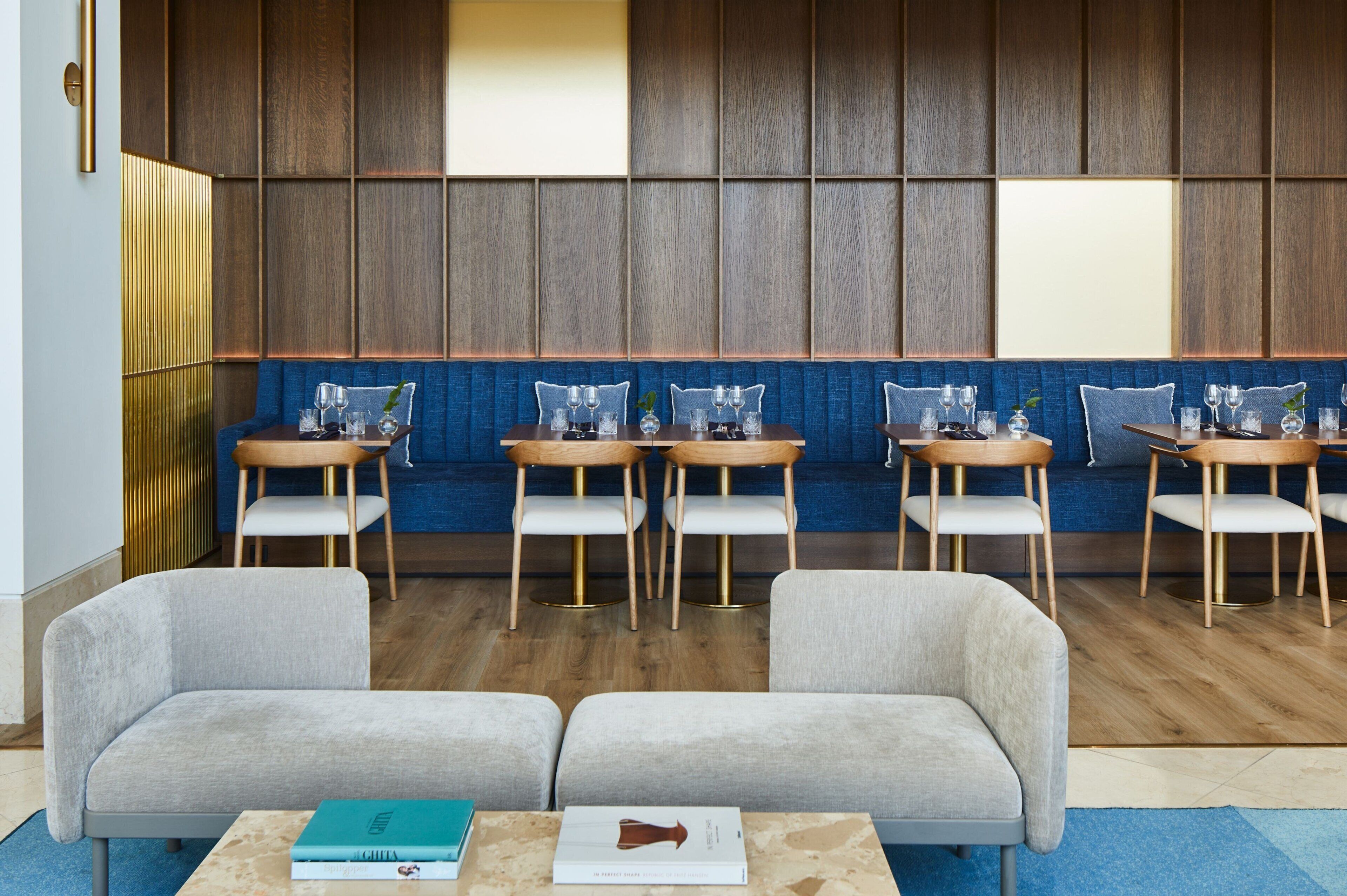 A modern waiting area with a wooden panel wall, blue cushioned seating, and a wooden coffee table with books.