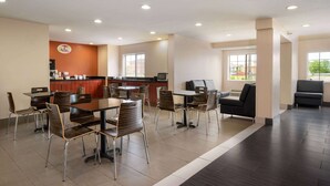 Un comedor espacioso con varias mesas y sillas, una zona de cocina con mostrador y electrodomésticos, y grandes ventanales que aportan luz natural.