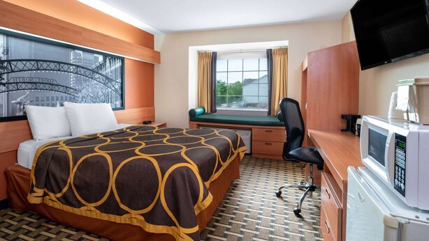 Habitación de hotel con cama, escritorio, silla, televisión y ventana con cortinas.