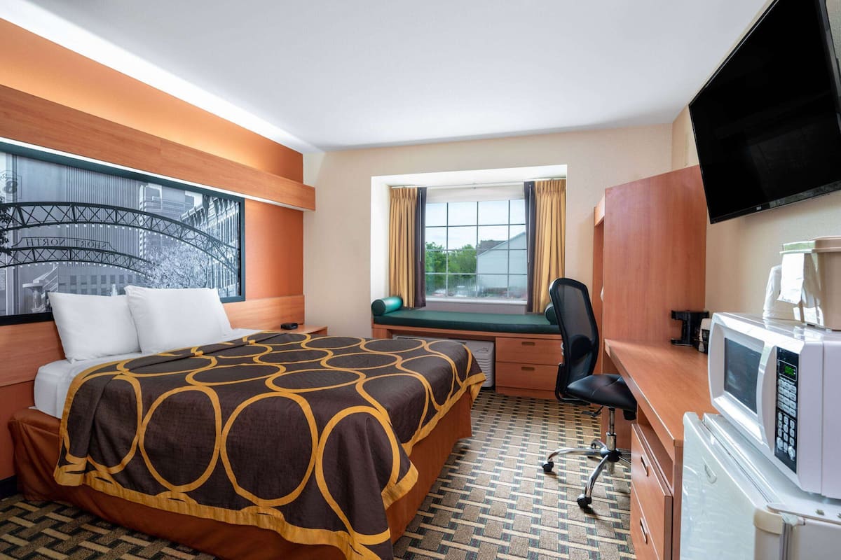 Una camera d'albergo con un letto, una scrivania, una sedia, una televisione e una finestra con tende.