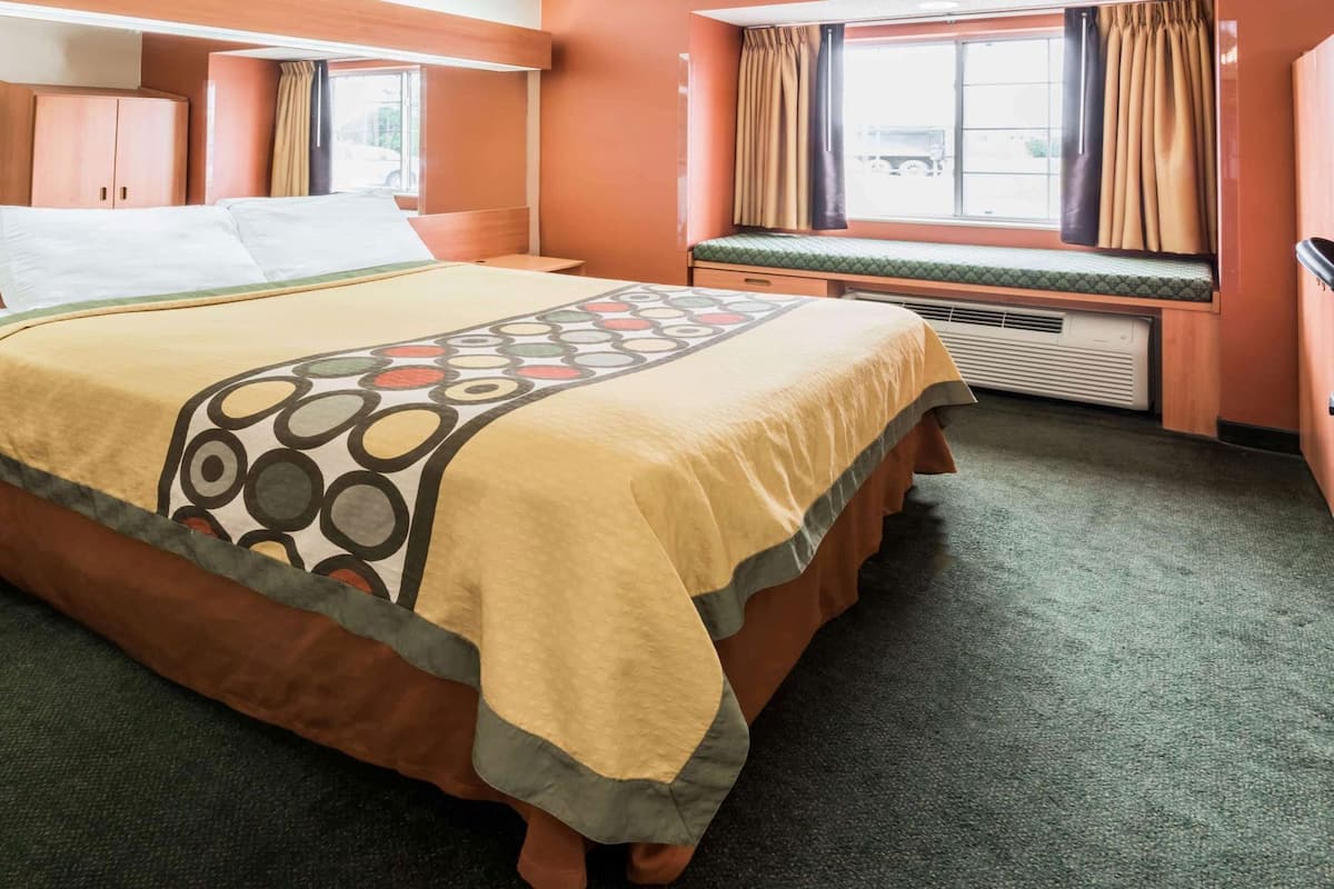 Una camera d'albergo con un letto, una finestra con tende, una panca e un armadio.