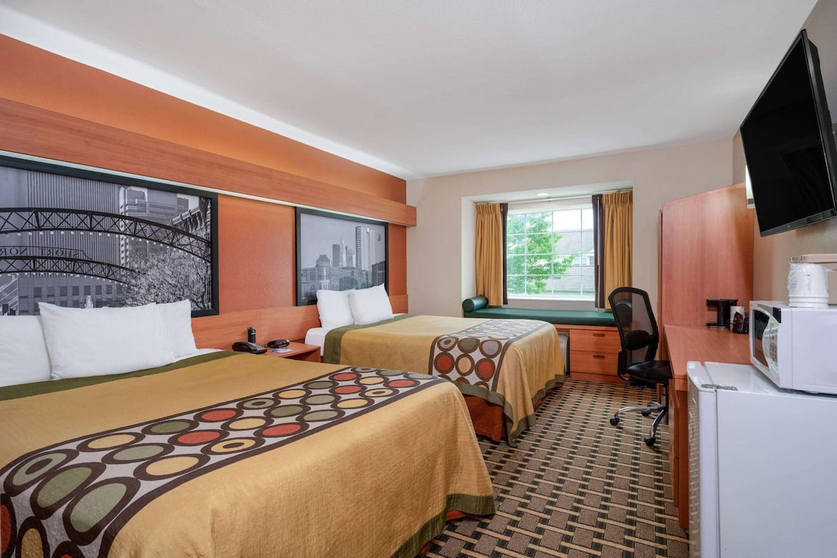 Una camera d'albergo con due letti, una scrivania, una sedia, una televisione e una finestra con tende.