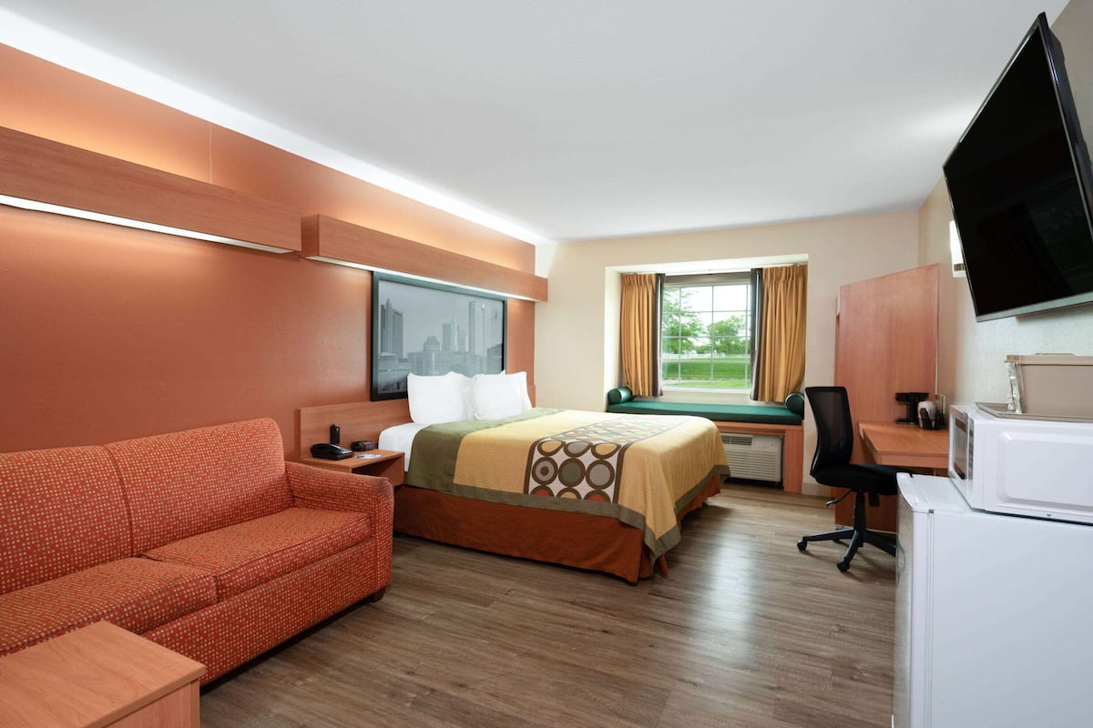 Una camera d'albergo con un letto, una scrivania, una televisione, un divano e una finestra con tende.