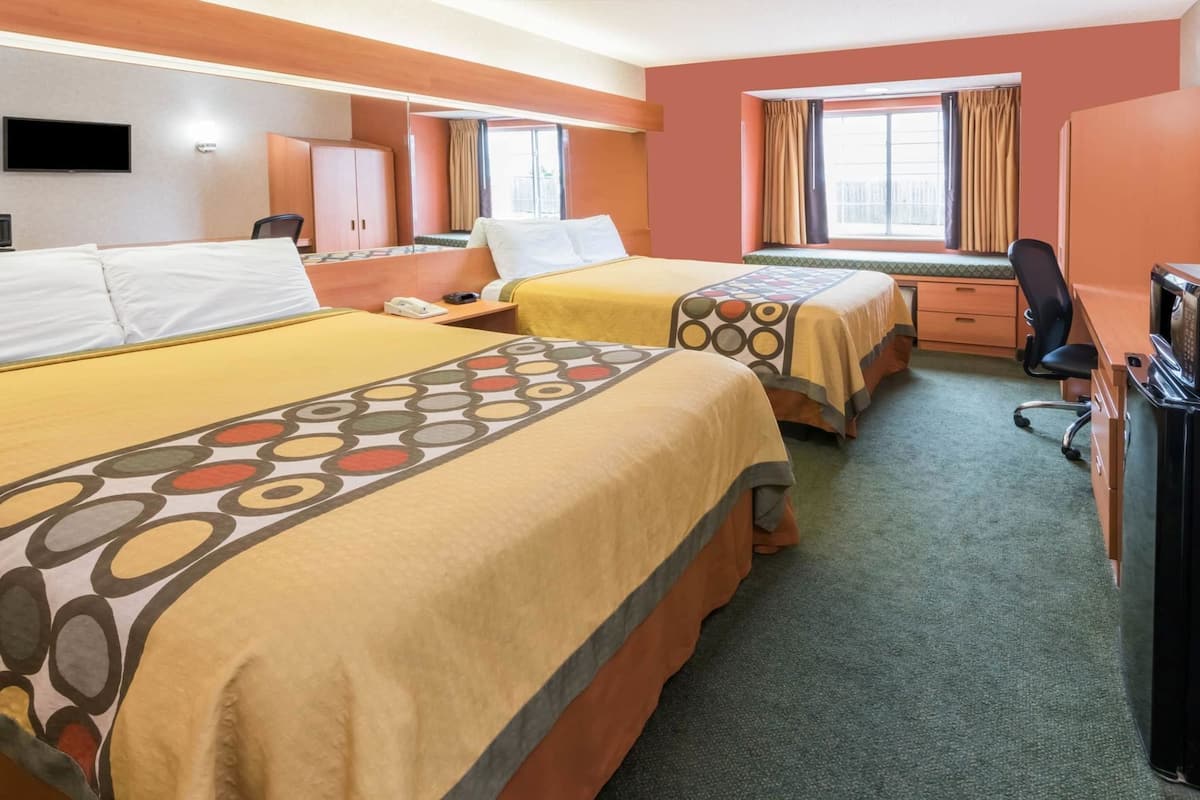 Camera d'albergo con due letti, una scrivania, una sedia, una televisione e una finestra con tende.