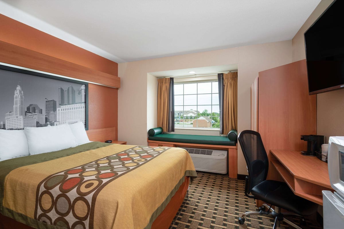 Una camera d'albergo con un letto, una scrivania, una sedia, una televisione e una finestra con tende.