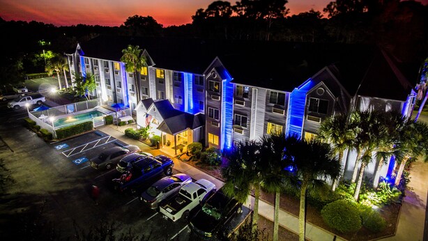 Un hotel con varias construcciones, piscina y estacionamiento con varios automóviles.