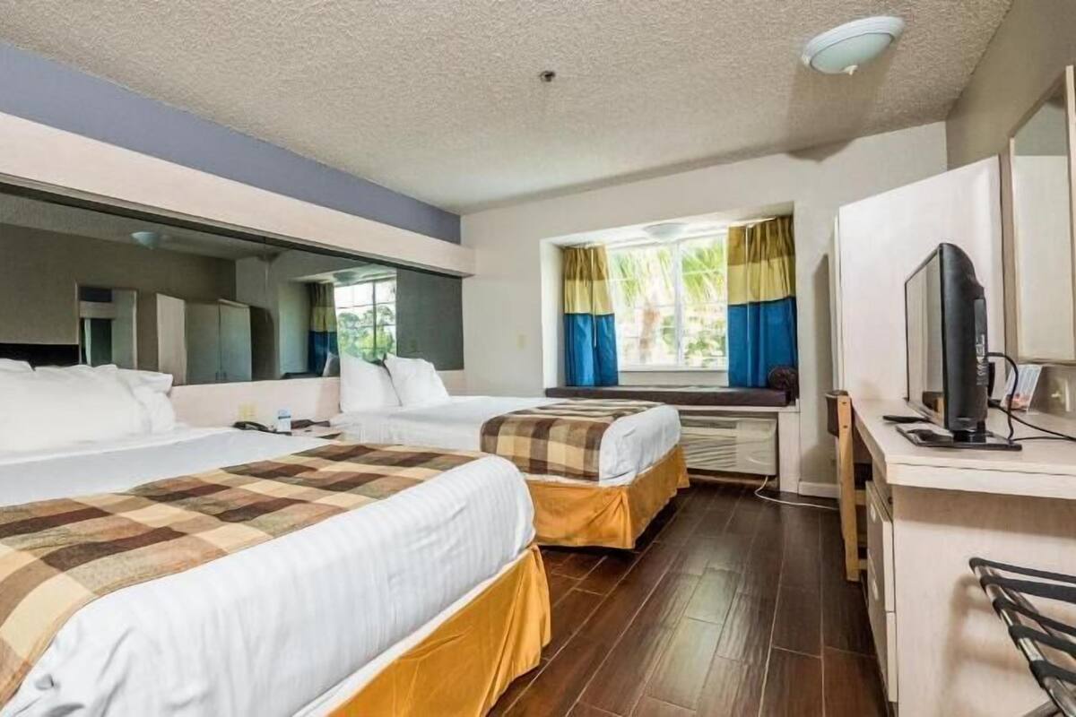 A hotel room with two beds, a desk, a TV, and a large window with curtains.