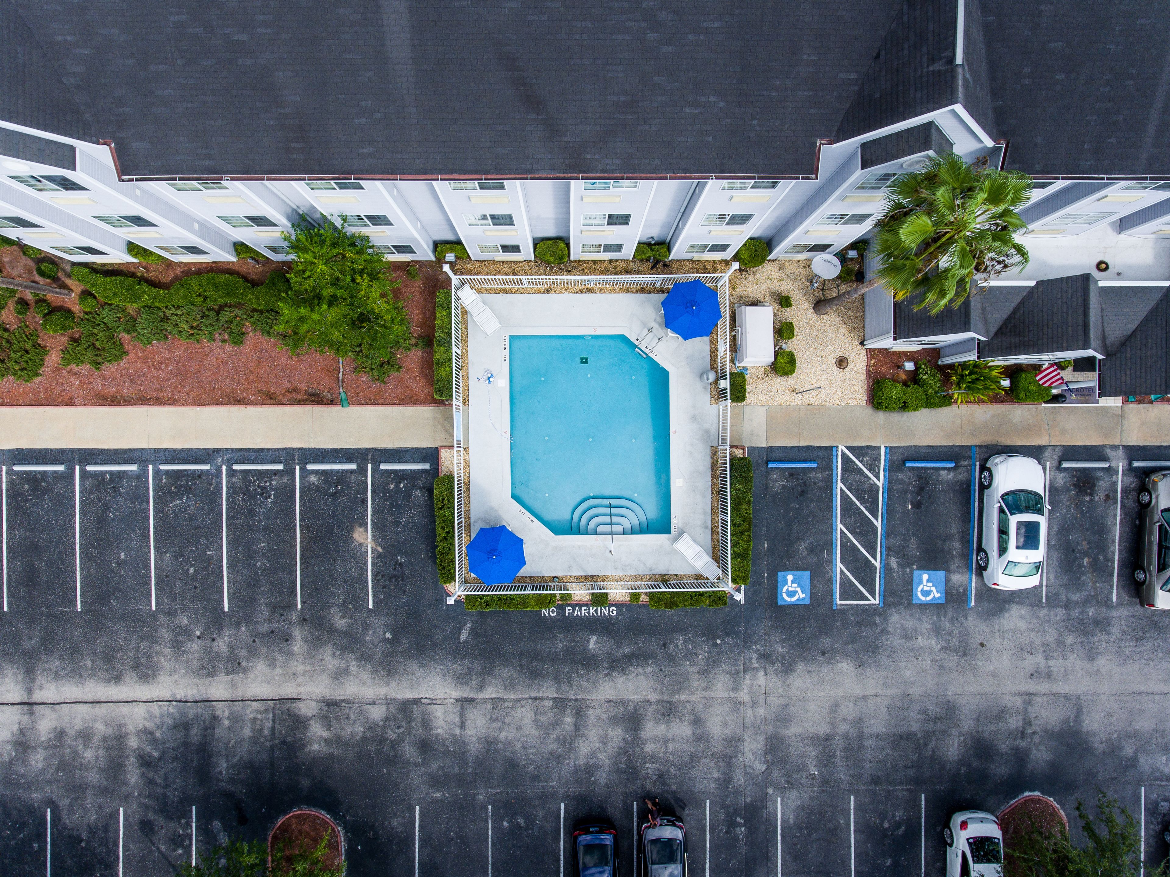 An aerial view of a hotel with a swimming pool, parking spaces, and a no parking sign.