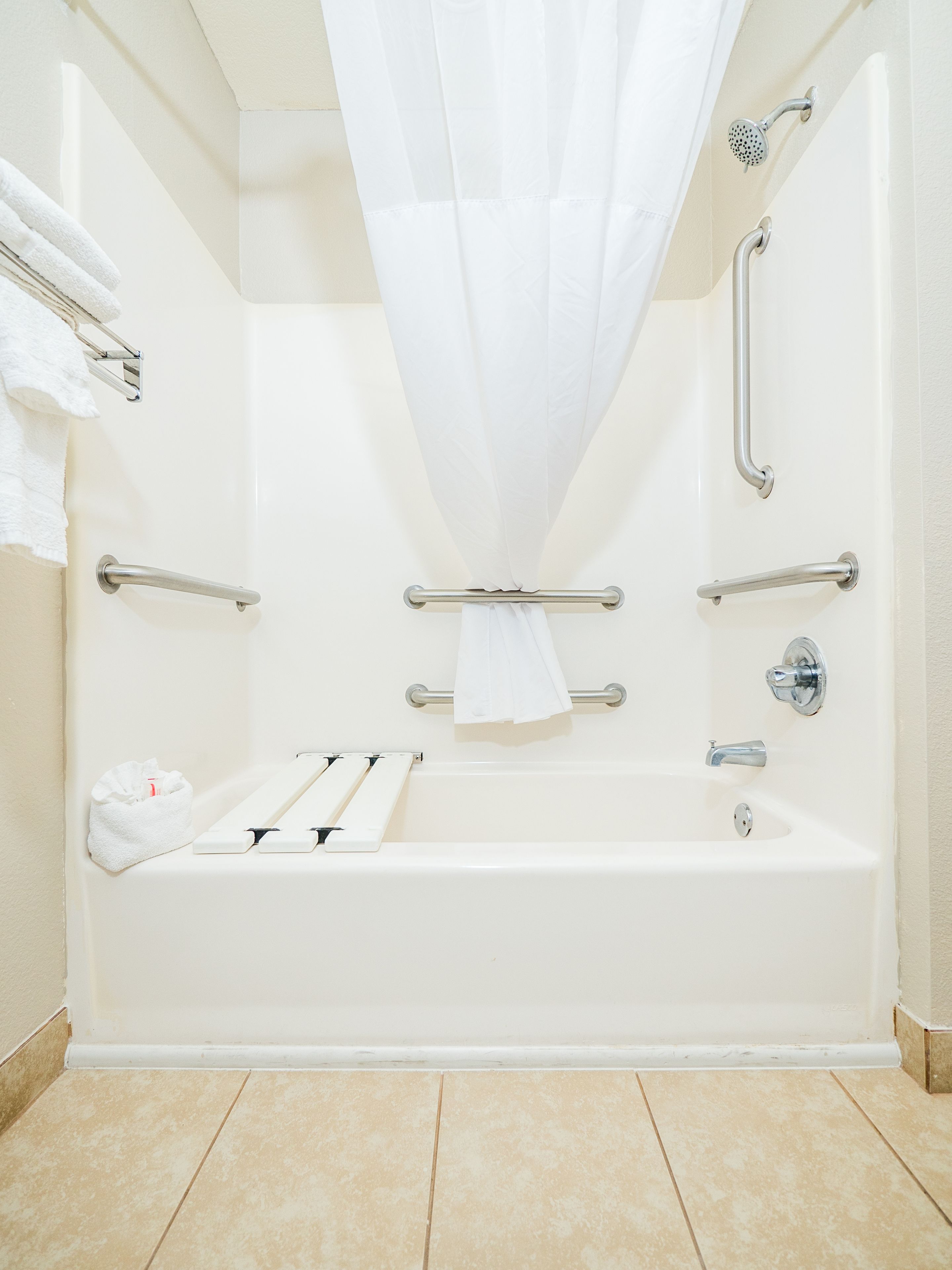 A white bathroom with a bathtub, grab bars, a showerhead, and a towel rack.