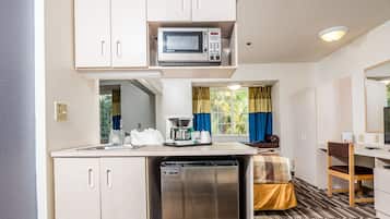 A compact kitchen with a microwave, a sink, and a dishwasher. There is a bed with a striped bedspread and a chair.