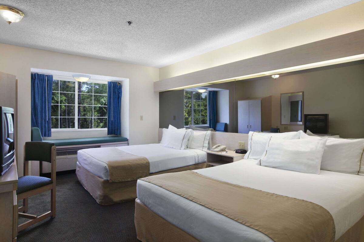 A hotel room with two beds, a desk, a chair, a TV, and a window with curtains.