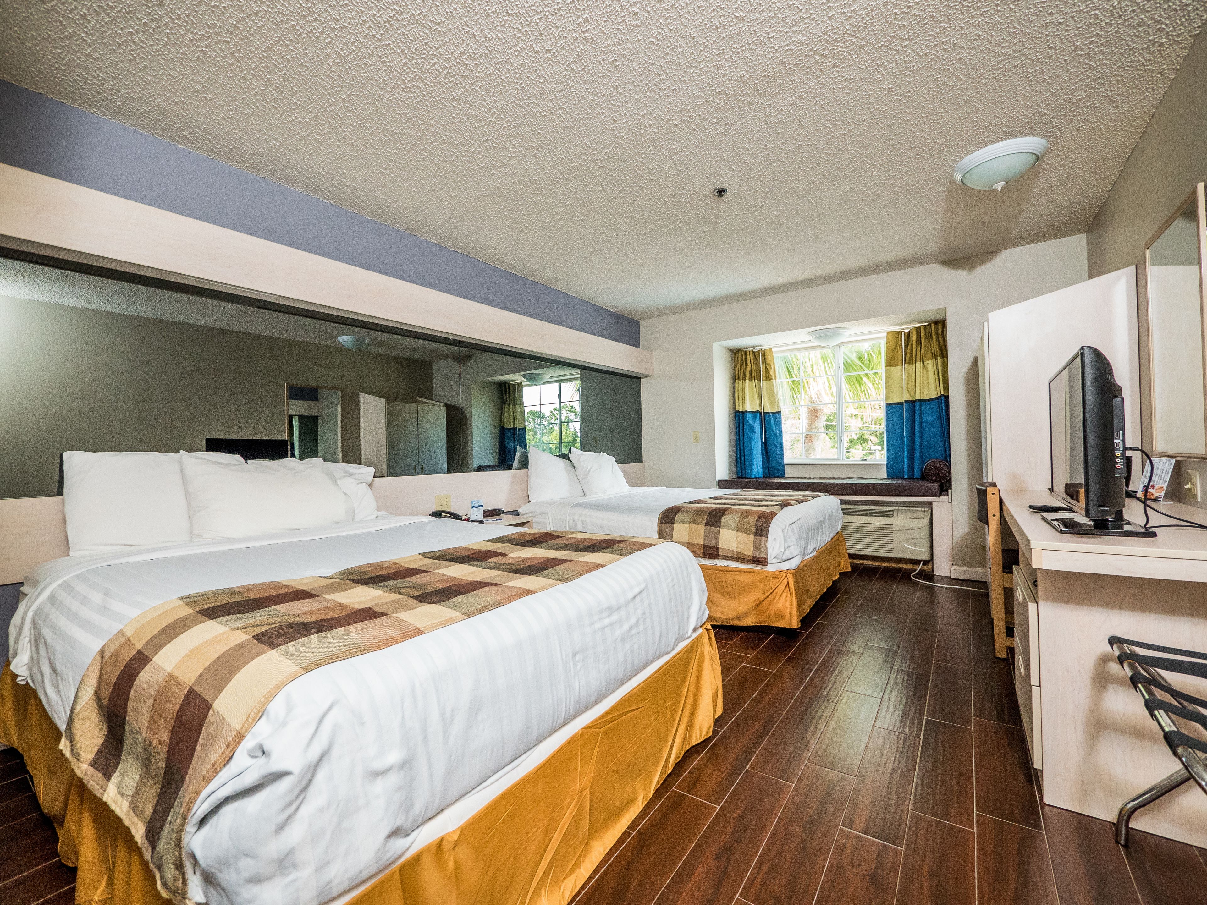 Habitació d'hotel amb dos llits, un escriptori amb un ordinador i una finestra amb cortines.