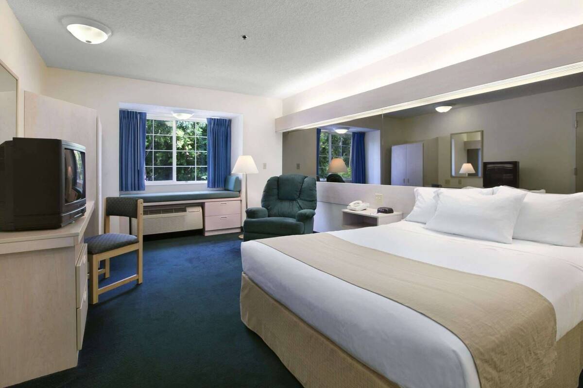 A hotel room with a bed, desk, chair, television, and windows.
