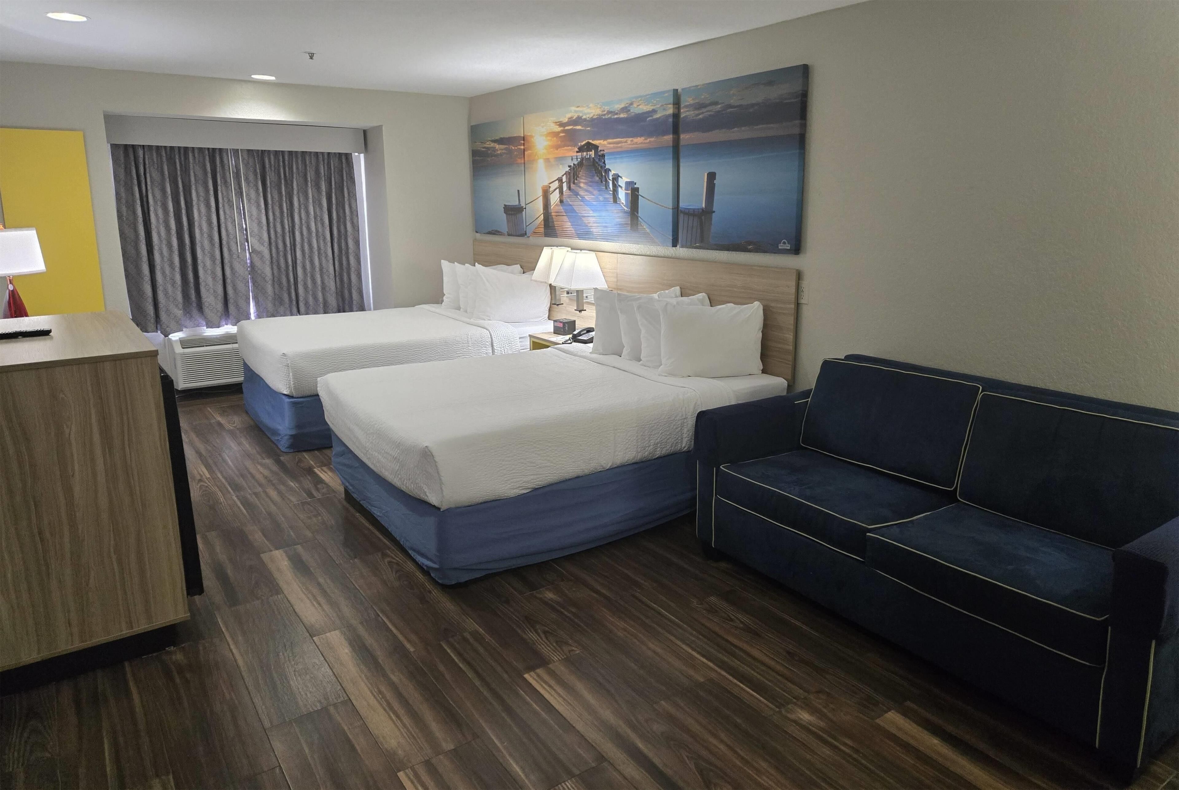A hotel room with two beds, a desk, a couch, and a large painting of a pier.