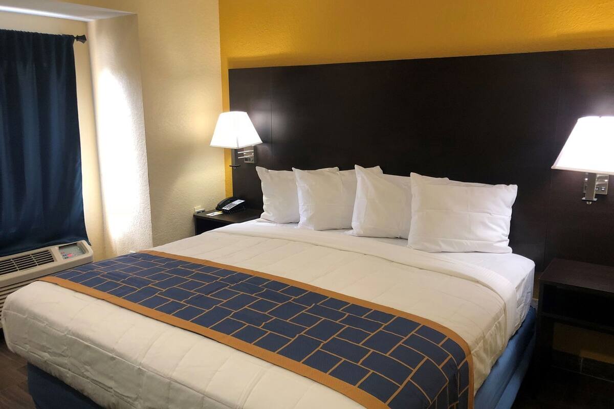 Habitación de hotel con una cama grande, dos lámparas de noche, un teléfono y una ventana con cortinas.