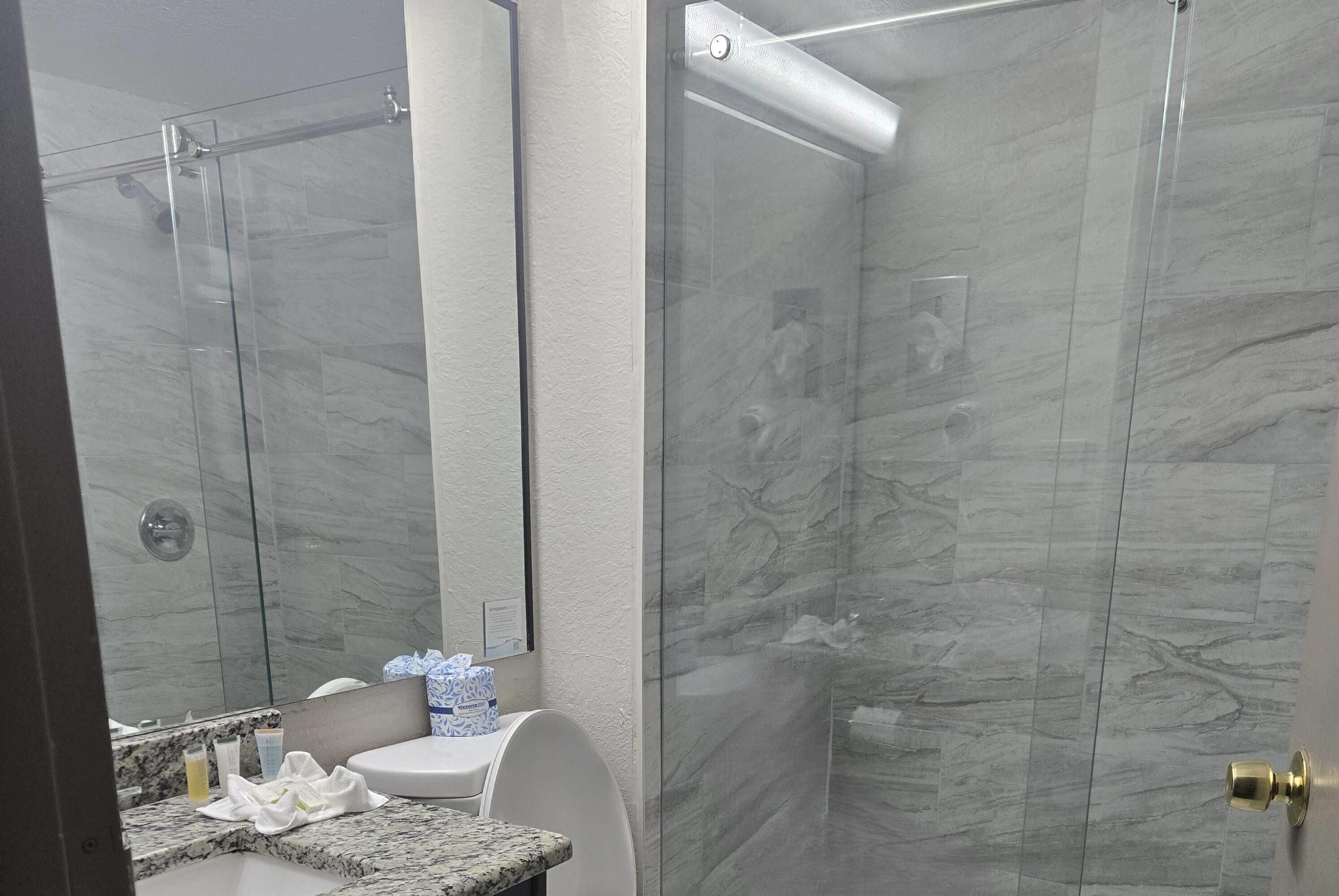 Et moderne badeværelse med et bruseafskærmning i glas, klinkegulv i marmor og en hvid vask med toiletartikler.