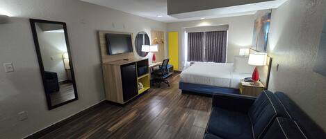 Habitación de hotel con cama, escritorio, silla, televisor, espejo y ventana con cortinas.