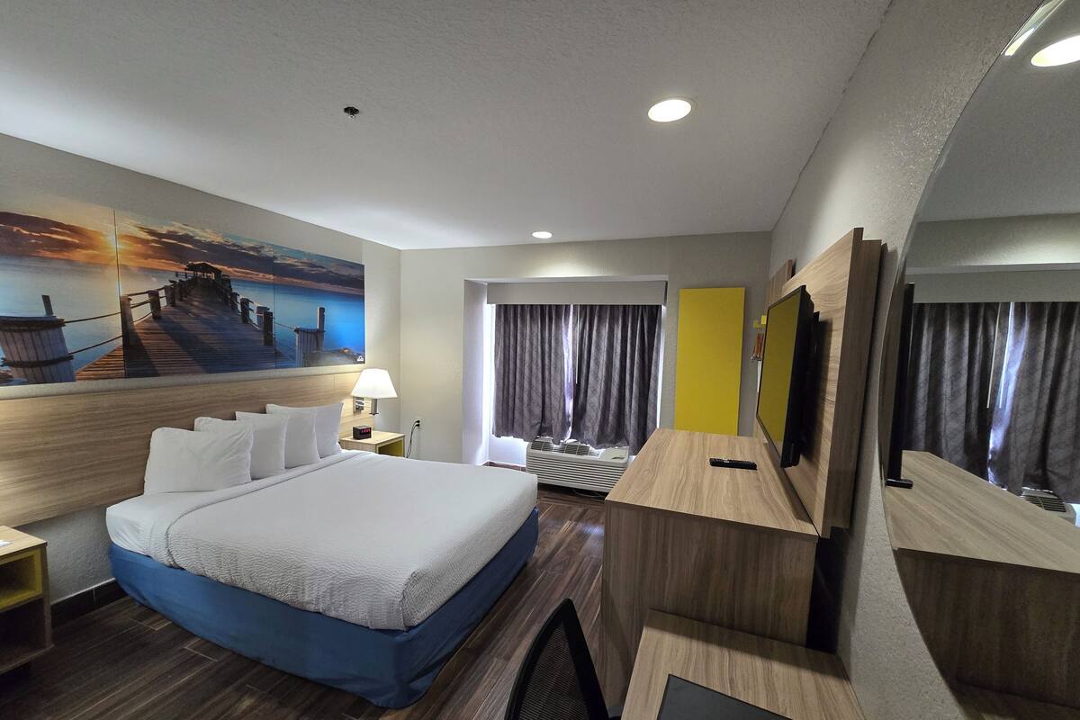 Habitación de hotel con cama, escritorio, silla, televisor y un cuadro en la pared.