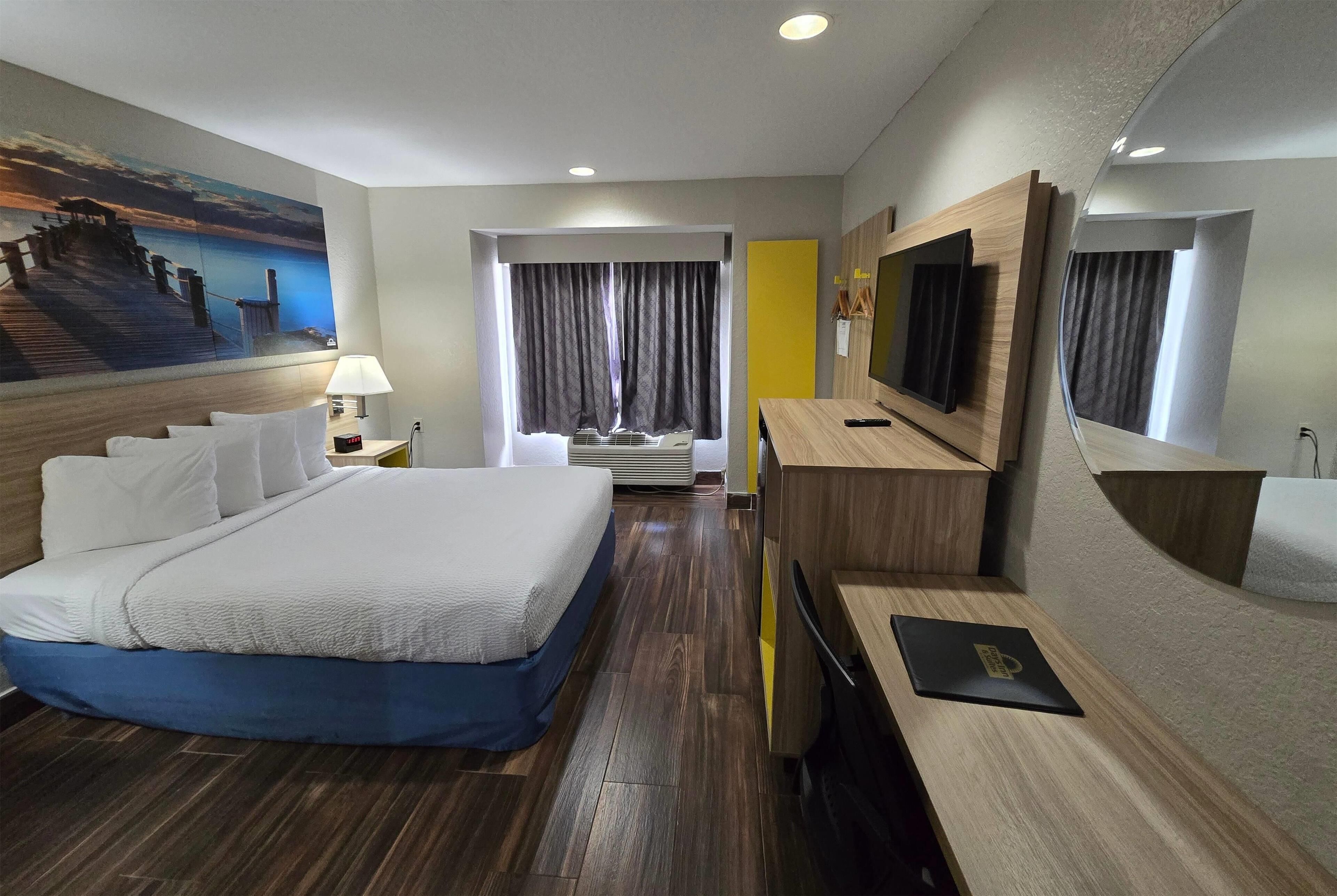 A hotel room with a large bed, a desk, a TV, and a painting of a pier.