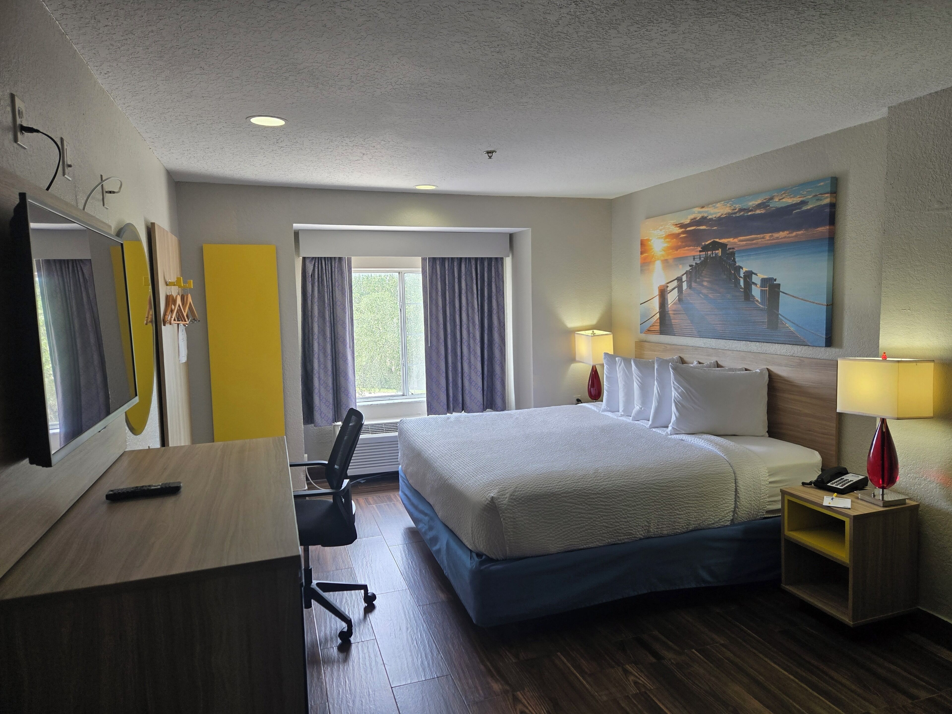 Een hotelkamer met een bed, bureau, stoel en een schilderij aan de wand.