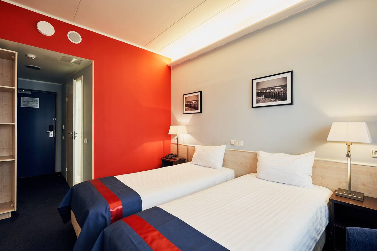 A hotel room with two beds, a red accent wall, and a wooden headboard.