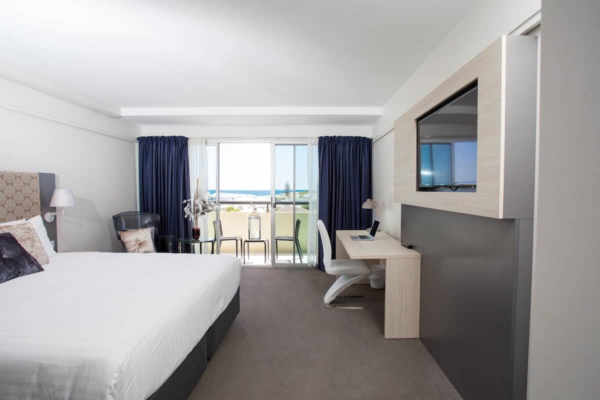A hotel room with a bed, desk, chair, and a large window with curtains.