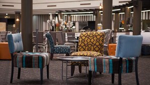 Un hall d’hôtel doté d’un espace salon comprenant des fauteuils et des poufs à motifs, une table ronde et un mur décoratif agrémenté de luminaires suspendus.