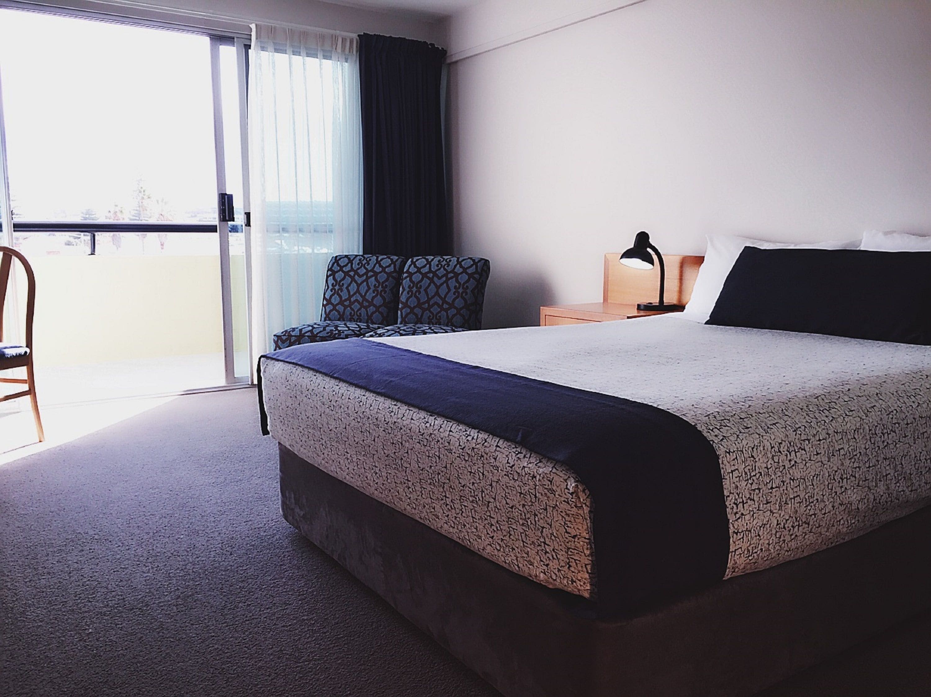 Habitación de hotel con una cama grande, una silla, un escritorio con lámpara y vistas a través de un ventanal.