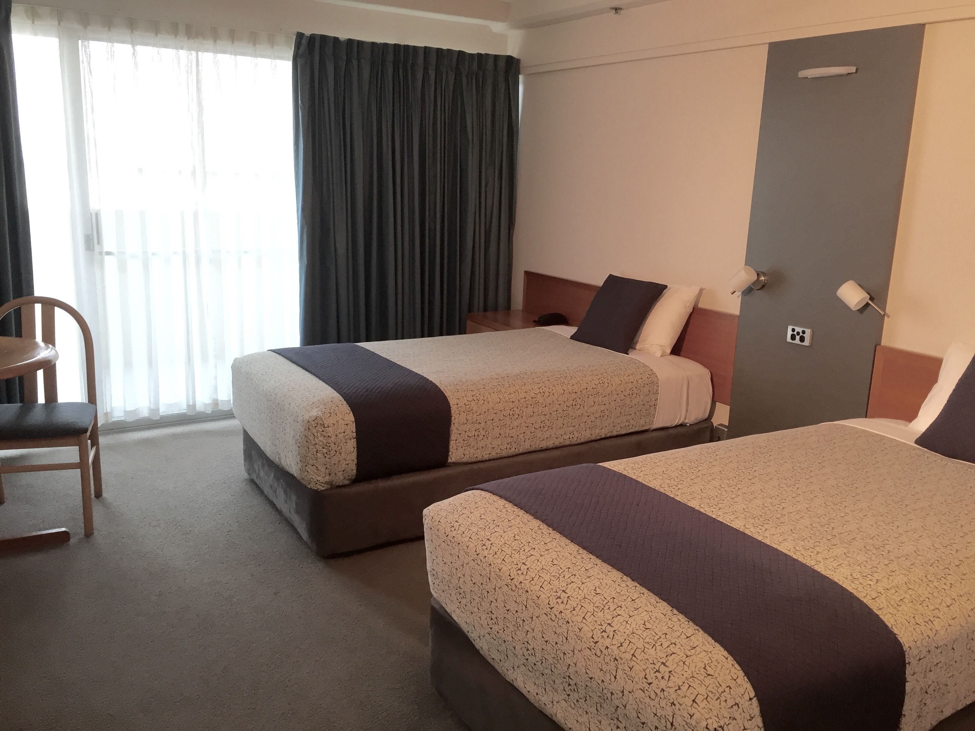 A hotel room with two beds, a chair, a door, and a window with curtains.