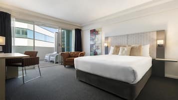 A hotel room with a large bed, a desk, two chairs, a view of the outside, and a modern headboard.